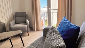 A living room with a grey armchair, a sofa with a blue cushion, and a small table. - Fifth Sense in Athens by ΜΡS (Athina)