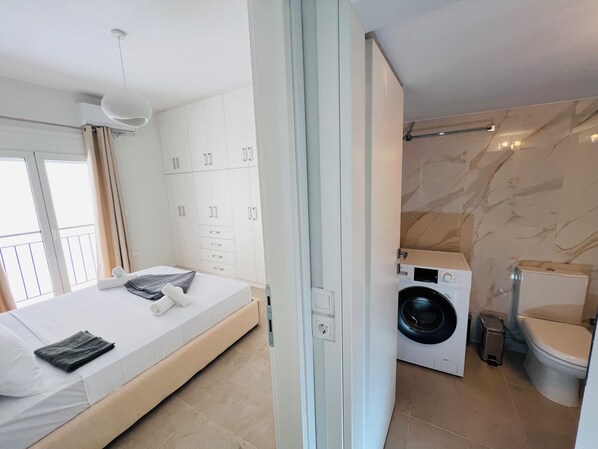 A bedroom with a bed, a wardrobe, a washing machine, and a toilet.