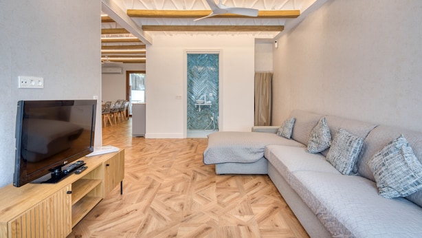 Una sala de estar moderna con televisor, sofá, piso de madera y ventilador de techo.