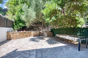Une terrasse en pierre avec un banc, entourée de verdure et d’un mur en pierre.