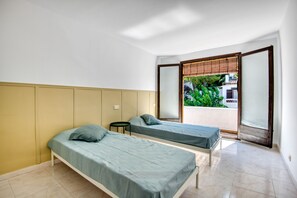 Une chambre avec deux lits simples, une petite table et une porte-fenêtre coulissante donnant sur un balcon.