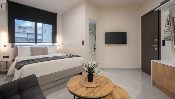 A modern bedroom with a bed, bedside table, and a TV mounted on the wall. - LIV - Comfortable Athens Studio S8-2A (Athens)
