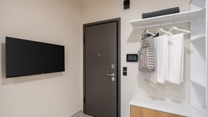 A modern room with a flat-screen TV mounted on the wall, a dark door, a white wardrobe with hanging clothes, and a small shelf with a towel. - LIV - Comfortable Athens Studio S8-2A (Athens)