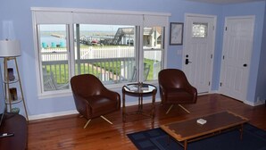 A room with two leather chairs, a small round table, a wooden coffee table, and a view of a white picket fence and a dock.