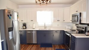 A modern kitchen with white cabinets, stainless steel appliances, and a wooden floor.