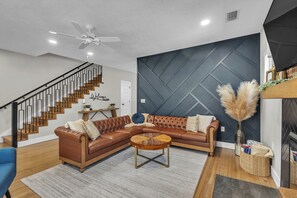 A modern living room with a sectional sofa, a round coffee table, a staircase with a black railing, and a decorative wall panel.