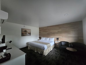 A modern hotel room with a bed, a desk, a chair, and a painting on the wall.