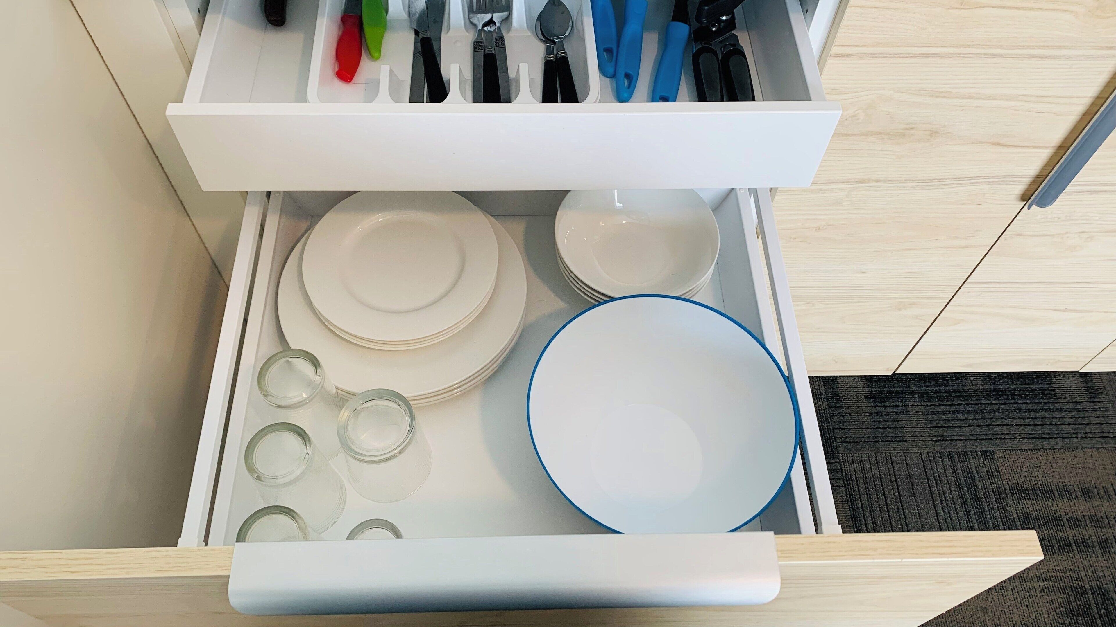 Un cajón con platos blancos, tazones y frascos de vidrio.