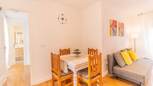 A room with a dining table, four wooden chairs, a sofa with cushions, and a wall clock. - Pyrenees Escape  with Terrace & BBQ (Sabiñánigo)