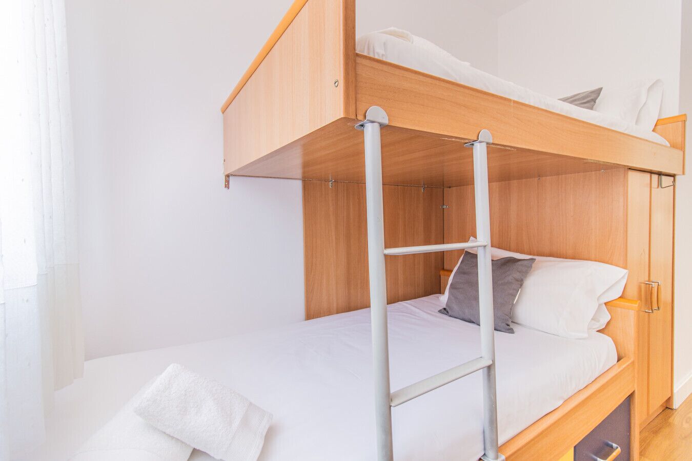 Una cama litera con escalera, ropa de cama blanca y una mesita de noche con lámpara.