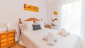 A neatly made bed with white linens and a gray pillow, a wooden nightstand with a lamp, and a painting of trees on the wall. - Pyrenees Escape  with Terrace & BBQ (Sabiñánigo)