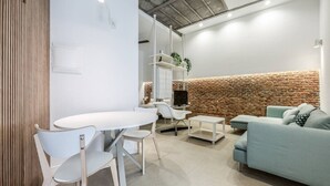 A modern living room with a white table, chairs, a light blue sofa, and a brick accent wall.