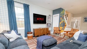 A living room with a large flat-screen TV, a wooden cabinet, and a colorful mural on the wall. - Private Cinema + Cowboy Pool, Putt Putt, Arcade (Indianapolis)