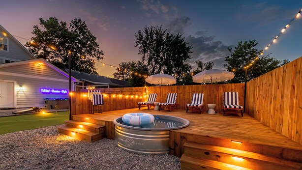 An outdoor hot tub area with wooden decking, lounge chairs, and string lights. - Private Cinema + Cowboy Pool, Putt Putt, Arcade (Indianapolis)