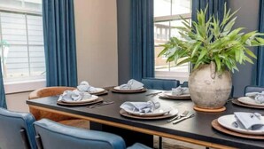 A dining area with a table set for six, blue chairs, a large potted plant, and a view of the outdoors through large windows. - Private Cinema + Cowboy Pool, Putt Putt, Arcade (Indianapolis)
