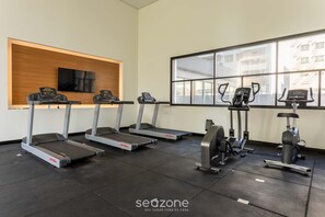A gym with treadmills, ellipticals, and a TV on the wall.