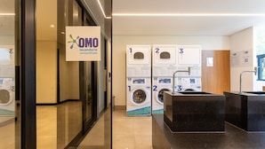 Ein moderner Waschraum mit drei Waschmaschinen, die mit 1, 2 und 3 beschriftet sind, und einem Schild für OMO Waschmittel.