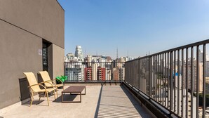 Eine Dachterrasse mit Blick auf eine Stadtlandschaft, mit einem modernen Gebäude, einer Brüstung und Gartenmöbeln.