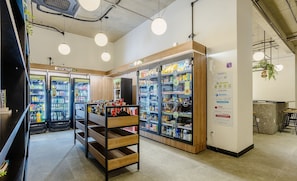 A modern retail space with refrigerated beverage dispensers, a wooden display shelf, and hanging pendant lights. - VNU - Apartamentos próximos de atrações em SP (São Paulo)