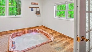 Una stanza spa con vasca idromassaggio, pavimento in legno e ampie finestre vista foresta.