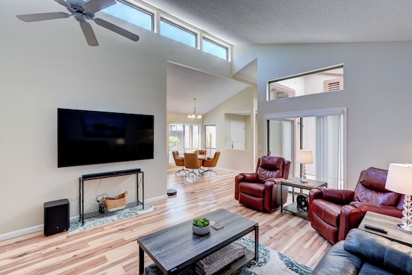 A spacious living room with a flat-screen TV, leather recliners, and a ceiling fan.