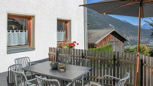 A patio with a table and chairs, a wooden fence, and a mountain view. - Ferienhaus S' Tobiasa (Schönwies)