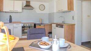 A compact kitchen with a stove, oven, and dishwasher. There's a dining table with breakfast items and a chair. - Ferienhaus S' Tobiasa (Schönwies)