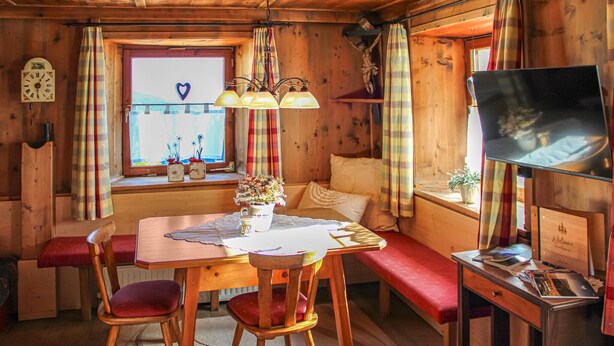 A cozy cabin interior with a wooden dining table, chairs, a bench, a television, and a window with curtains. - Ferienhaus S' Tobiasa (Schönwies)