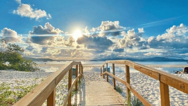 A wooden boardwalk leading to a beach with a clear sky and sun. - Beautiful Apartments Close to the Beach Stacy (Florianópolis)