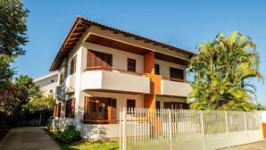 A two-story residential building with a balcony, a white fence, and a well-maintained lawn. - Beautiful Apartments Close to the Beach Stacy (Florianópolis)