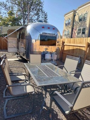 A recreational vehicle with a 'RESTREAM' sign, a metal table with chairs, and a wooden fence in the background.