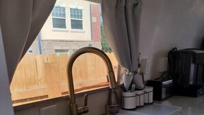 Une cuisine avec un évier à deux bacs, une clôture en bois à l’extérieur et une fenêtre avec des rideaux.