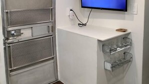 Une pièce avec un téléviseur diffusant Disney+, un meuble métallique avec des tiroirs, une étagère avec des verres et un tapis à motifs.