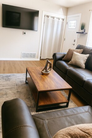 Un salon avec une table basse en bois, un canapé en cuir et un téléviseur fixé au mur.