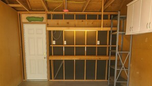 A garage with a concrete floor, wooden beams, a white door, and metal shelving units. - Applewood Charming Two Bedroom Big Fenced Yard (Fort Collins)