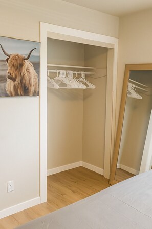 Une chambre à coucher avec un placard contenant des cintres blancs et un miroir.