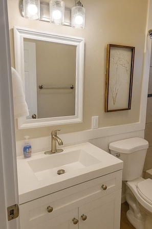 Une salle de bain avec un meuble-lavabo blanc, un grand miroir, une estampe botanique encadrée et des toilettes.