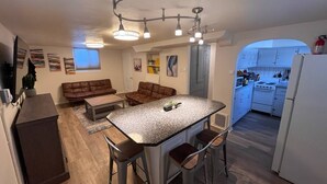 A compact kitchen with a central island, bar stools, a dining area with a brown leather couch, and a kitchenette in the background.