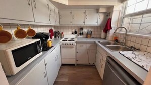 A compact kitchen with white cabinets, a microwave, stove, sink, and a dishwasher.