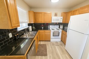 A kitchen with wooden cabinets, a black tiled backsplash, a white stove, and a white refrigerator.