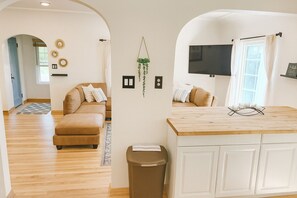 Ein modernes Wohnzimmer mit einem beigefarbenen Sofa, einem Holztisch und einem an der Wand befestigten Fernseher.