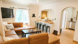 Un salon moderne avec un canapé, une table basse et un téléviseur. Il y a également un coin cuisine avec un comptoir et des chaises.