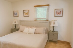 A bedroom with a large bed, two bedside tables with lamps, a window with blinds, and three framed butterfly pictures on the wall. - Adorable house next to campus (Fort Collins)