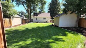 Un jardin avec une pelouse bien entretenue, une clôture en bois et une maison en arrière-plan.