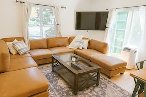 A modern living room with a sectional sofa, a glass coffee table, and a flat-screen TV mounted on the wall.