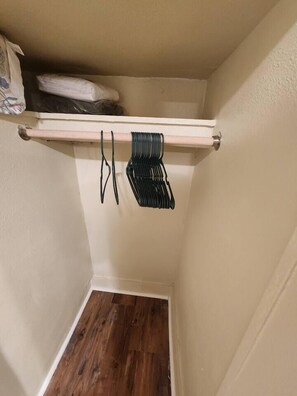 Un petit placard de rangement avec une étagère en bois, une tringle pour suspendre les vêtements et une porte blanche.