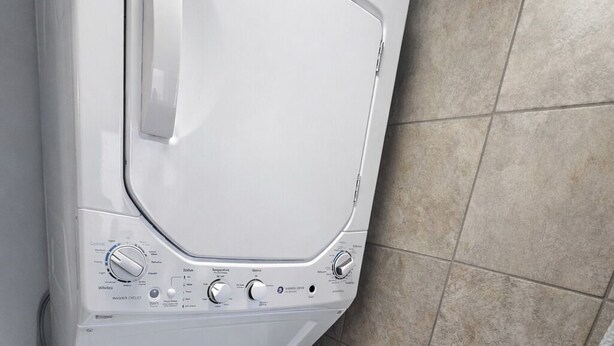 A front-loading washing machine with a control panel, a dryer below, and a tiled floor.