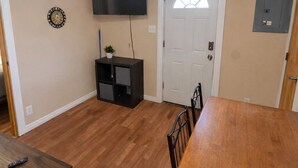 A dining area with a wooden table and chairs, a television mounted on the wall, and a door with a window.