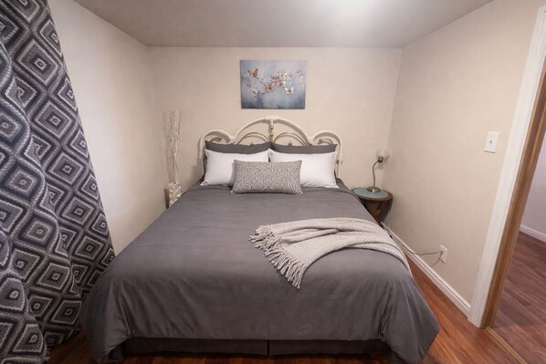 Une chambre à coucher comprenant un lit, une table de chevet, une œuvre d’art murale et un rideau à motifs.