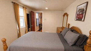 A bedroom with a wooden bed, a nightstand, a mirror, and a door leading to another room.